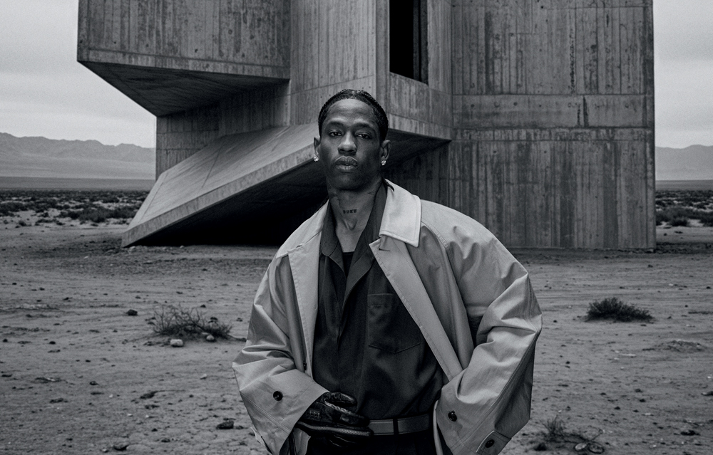 Portrait de Travis Scott en noir et blanc, regardant la caméra au milieu d’un paysage désertique.