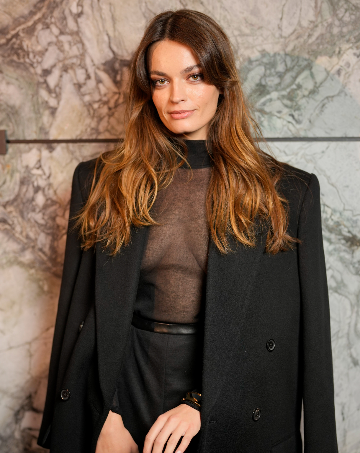 À l'affiche du film Le Monde de Narnia, l'actrice Emma Mackey prend la pose sur le photocall d'un défilé dans un costume noir et top en dentelle.